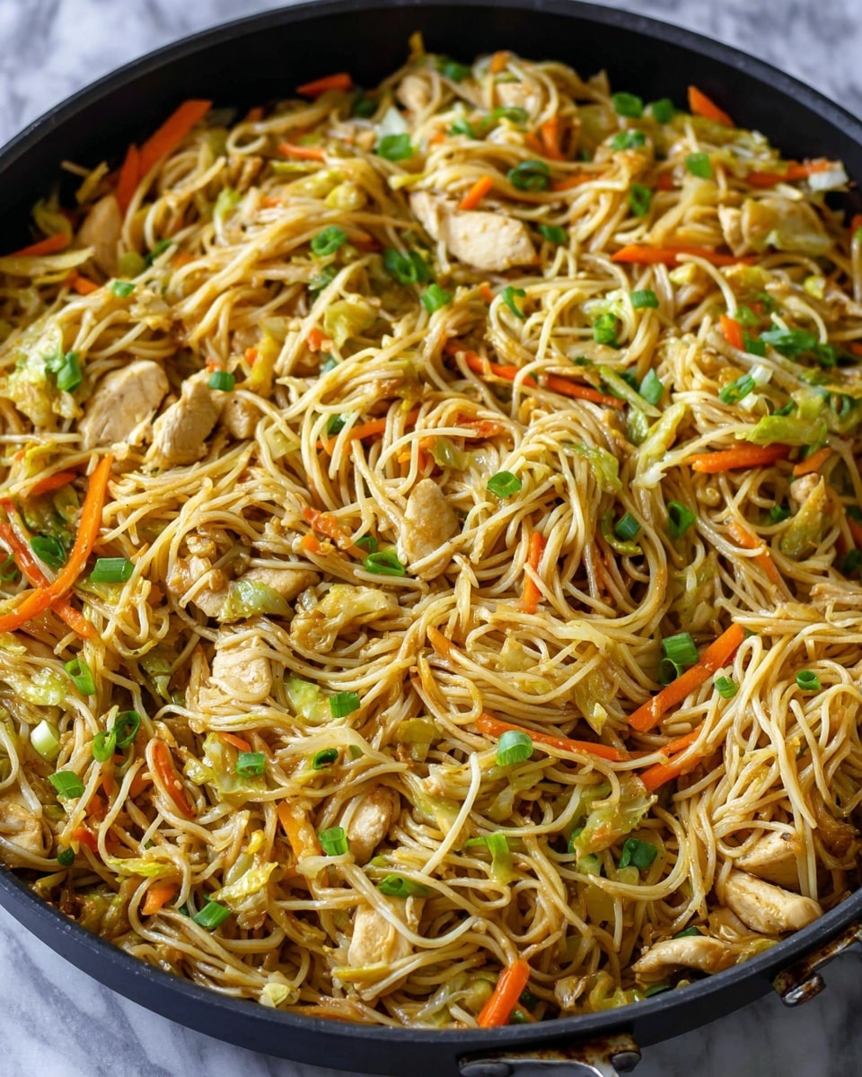 A large black pan filled with stir-fried noodles that look thin and light brown, mixed with small pieces of light-colored cooked chicken, thin orange carrot sticks, chopped light green cabbage, and green onion slices scattered throughout. The noodles and vegetables are shiny, showing they are cooked with sauce, with a mix of smooth and slightly soft textures. The pan is sitting on a white marbled surface. Photo taken with an iphone --ar 4:5 --v 7