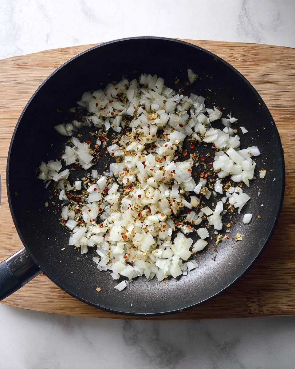 A black pan filled with a single layer of chopped white onions mixed with small red and green spices, slightly cooked and scattered unevenly inside the pan; the pan is set on a light wooden surface replaced by a white marbled texture. photo taken with an iphone --ar 4:5 --v 7