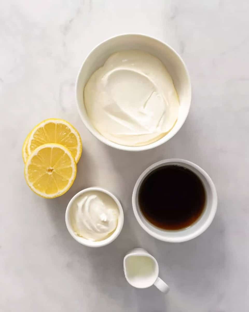 The image shows five items placed on a white marbled surface: a large white bowl filled with smooth white cream at the top center, a smaller white bowl with a thick white cream below and to the left of it, two lemon halves with bright yellow skin and pale yellow flesh beside each other slightly to the right, a tiny white container with a small amount of clear liquid near the bottom left, and a white measuring cup filled with dark brown liquid located at the bottom right. The items are arranged in a loose circle, with clear textures visible in the creams and lemon flesh, all captured in natural lighting. Photo taken with an iphone --ar 4:5 --v 7