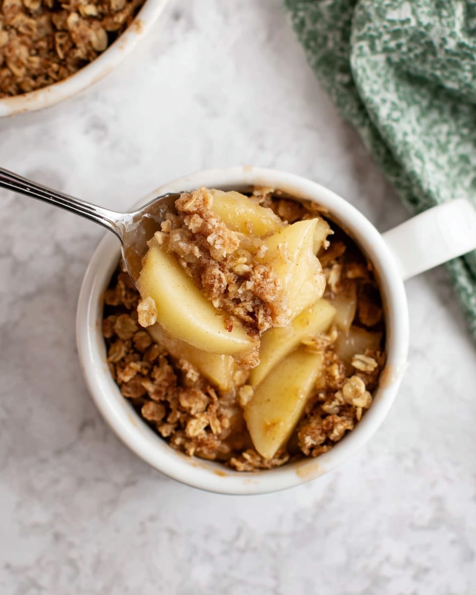 The image shows a small white pot filled with apple crisp dessert. The dessert has two visible layers: the bottom layer is soft cooked apple slices in light yellow, and the top layer is a crumbly oat and cinnamon mix in light brown. A silver spoon holds a scoop of the dessert above the pot, showing both the apple slices and the crunchy oat topping. The pot is set on a white marbled surface, and part of a green and white cloth is in the top right corner of the image. The mood is bright and cozy. Photo taken with an iphone --ar 4:5 --v 7