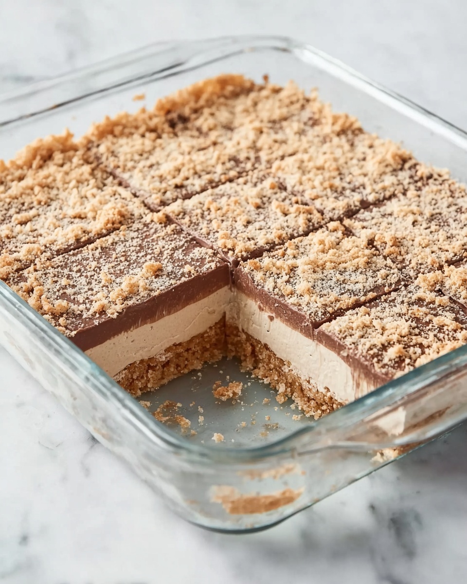 Disneyland Peanut Butter Squares Recipe 5 The image shows a clear rectangular glass dish with a dessert made of four distinct layers. The bottom layer is a light tan color with a crumbly texture, followed by a thicker creamy brown layer. Above that is a thinner, darker brown layer with a smooth texture, topped with a final layer that looks like finely crushed crumbs, light beige in color, spread evenly on top. Part of the dessert is missing from the bottom right corner, showing the clean edges of each layer. The dish is placed on a white marbled surface. Photo taken with an iphone --ar 4:5 --v 7