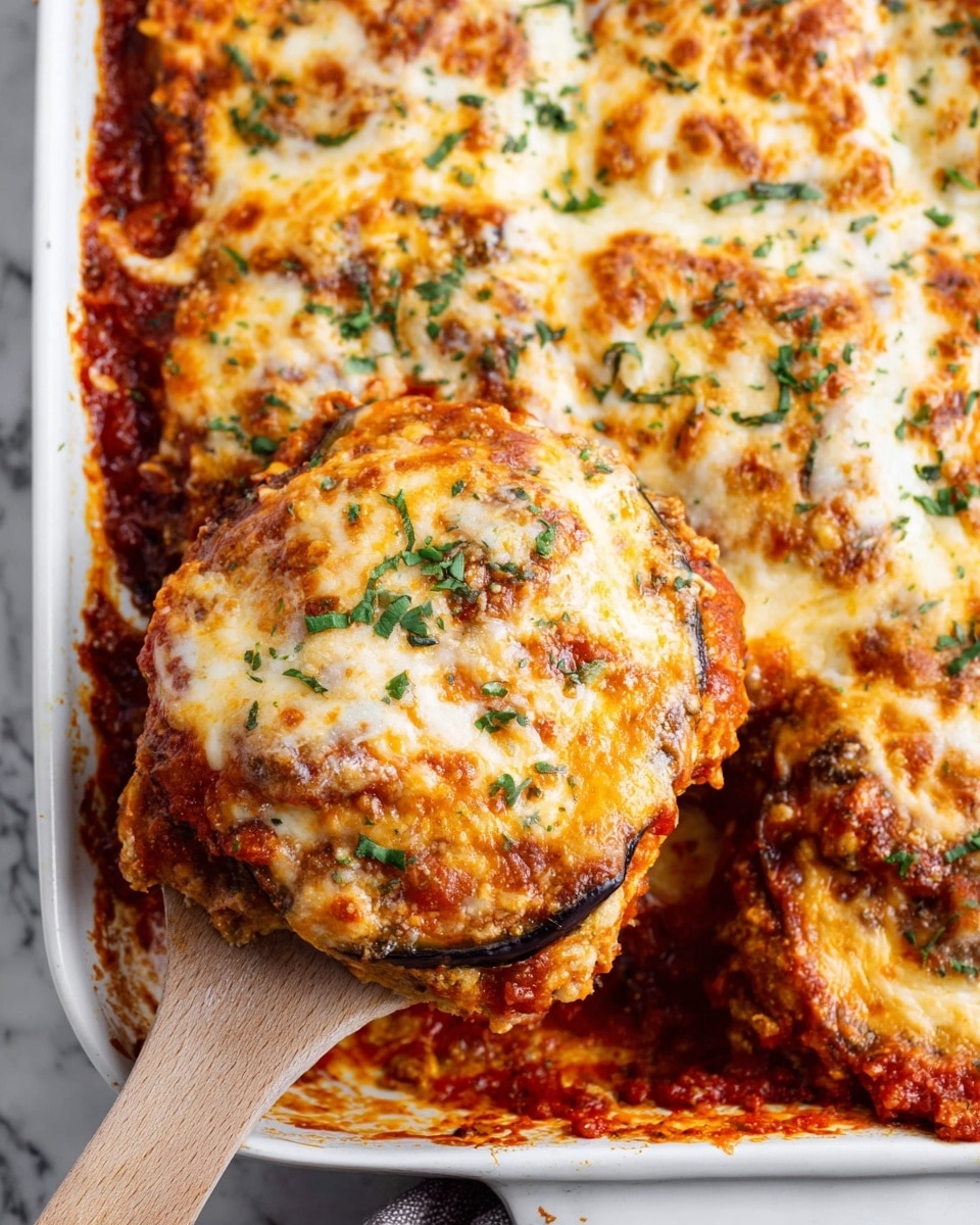 The image shows a close-up of a white baking dish filled with layered eggplant parmesan. The bottom layer is thick, dark red tomato sauce spreading along the edges. On top of the sauce, there are multiple herb-sprinkled layers of golden melted cheese with a slightly brown, bubbly texture. Under the cheese are slices of tender, cooked eggplant with a rich orange and brown tone visible where a large piece is lifted out with a wooden spatula. Fresh small green herb pieces are scattered across the top cheese layer, adding a touch of color. The dish sits on a white marbled surface. photo taken with an iphone --ar 4:5 --v 7