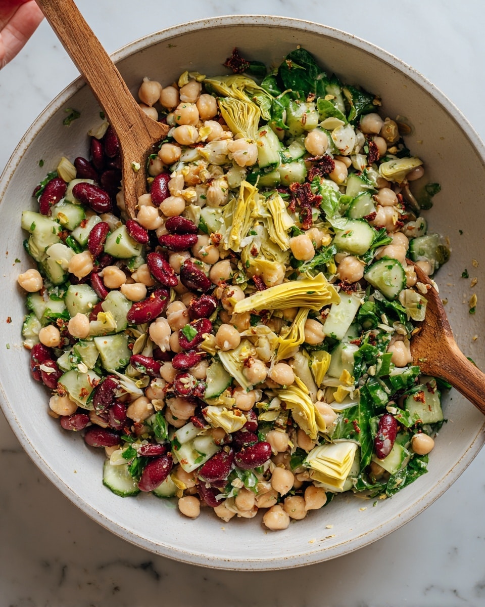 A large white bowl filled with a colorful bean salad, showing three main layers: the bottom layer with chickpeas and white beans, the middle layer with kidney beans and sliced cucumber, and the top layer with green leafy herbs and thin yellow artichoke pieces. The salad looks fresh with pieces of sun-dried tomatoes scattered throughout. Two wooden spoons are placed in the bowl, one submerged in the salad on the left and another held by a woman's hand on the right side. The bowl sits on a white marbled surface. photo taken with an iphone --ar 4:5 --v 7