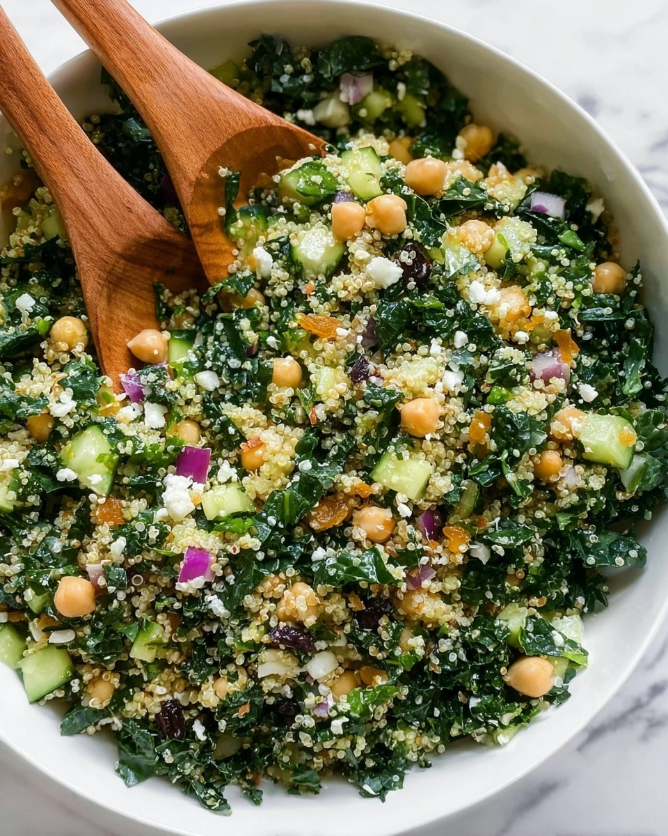 A white bowl filled with a mixed salad showing many layers: chopped dark green kale leaves form the base, topped with light yellow-beige quinoa scattered evenly, bright green cucumber pieces, pale beige chickpeas, small orange raisins, and tiny white cheese crumbles mixed throughout. Small diced purple onions and green herbs are visible, adding color and texture. Two wooden spoons with smooth grain rest inside the bowl on the salad, partially digging into the mix. The background features a white marbled texture. photo taken with an iphone --ar 4:5 --v 7