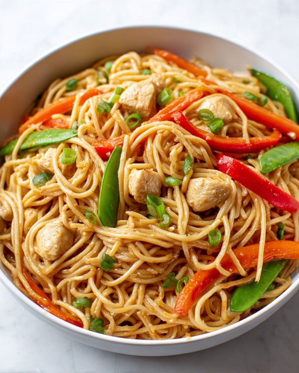 A white bowl filled with light brown noodles as the main layer, mixed with small light beige pieces of cooked chicken throughout. Bright red bell pepper strips and orange carrot sticks are scattered in the noodles. Green snap peas and small chopped green onions add color on top and between the noodles. The whole dish looks shiny and fresh, sitting on a white marbled surface. Photo taken with an iphone --ar 4:5 --v 7