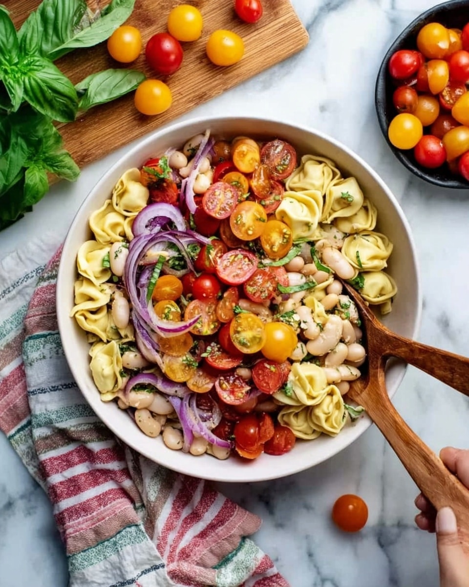 The image shows a white bowl filled with a colorful pasta salad on a white marbled surface. The salad has three layers of ingredients: the bottom layer is a mix of small white beans and green herbs, the middle layer is yellow tortellini pasta, and the top layer consists of halved red and yellow cherry tomatoes and thin slices of purple onion. Two wooden spoons are placed inside the bowl, with one woman's hand gently holding one spoon on the right side of the bowl. Around the bowl, there are scattered yellow and red cherry tomatoes on a wooden board and a striped cloth, along with fresh green basil leaves at the top left. A small black bowl filled with more red and yellow cherry tomatoes is placed at the top right corner. photo taken with an iphone --ar 4:5 --v 7