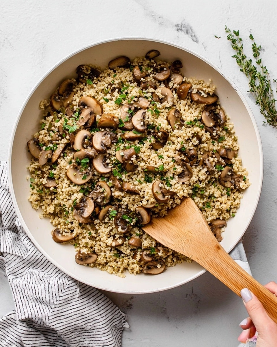 A white pan filled with a mix of cooked grains and sliced mushrooms in a light brown color, sprinkled with small pieces of green herbs throughout. The grains look fluffy and soft, while the mushrooms have a smooth, slightly shiny texture. A wooden spatula with a light brown handle is resting inside the pan, with a woman's hand holding the handle. The pan is placed on a white marbled surface, and there are small green herb sprigs on the surface near the pan. A white and gray striped cloth is also visible near the pan edge. photo taken with an iphone --ar 4:5 --v 7