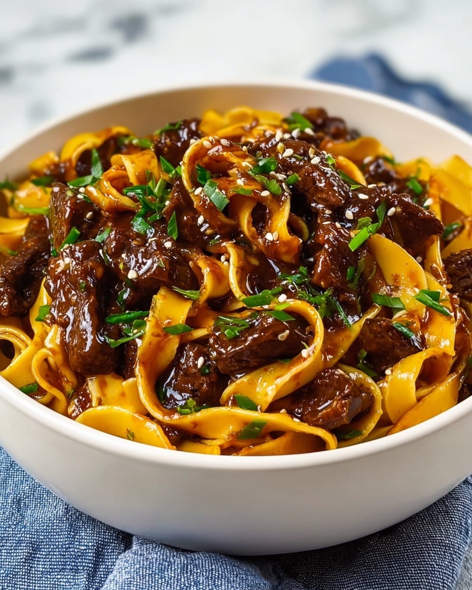 A white bowl filled with a rich dish made of wide, flat yellow noodles mixed with dark brown chunks of meat coated in a shiny sauce. Green chopped herbs and small sesame seeds are scattered on top, adding pops of color. The noodles and meat are layered evenly, giving the dish a hearty look. The bowl sits on a blue and white cloth, with a white marbled surface in the background. photo taken with an iphone --ar 4:5 --v 7