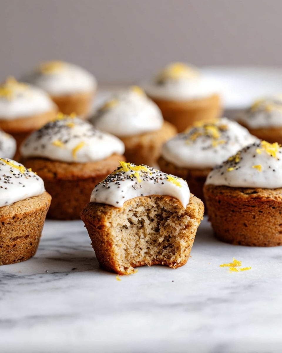 A group of light brown muffins are placed on a white marbled surface, with most muffins topped with a smooth white frosting sprinkled with small black seeds and a few yellow zest pieces. One muffin in the front has a bite taken out of it, showing its soft, moist interior with a crumbly texture. The muffins have a slightly rough surface and are arranged in loose clusters, with the white frosting layer sitting unevenly on top of each muffin. The background is blurred, keeping focus on the muffins. photo taken with an iphone --ar 4:5 --v 7