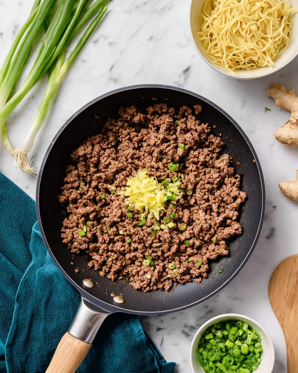 A black frying pan with cooked brown minced meat spread evenly inside, with two small piles of finely chopped yellow and light green ginger placed in the center on top of the meat. Around the pan, there is a white marbled surface holding three fresh green onions at the top left, a small white bowl with bright green chopped spring onions in the bottom right, some ginger root pieces nearby, and a white bowl with pale yellow cooked noodles on the top right. A wooden spatula is partly covered by a dark teal cloth underneath the frying pan's handle. Photo taken with an iphone --ar 4:5 --v 7