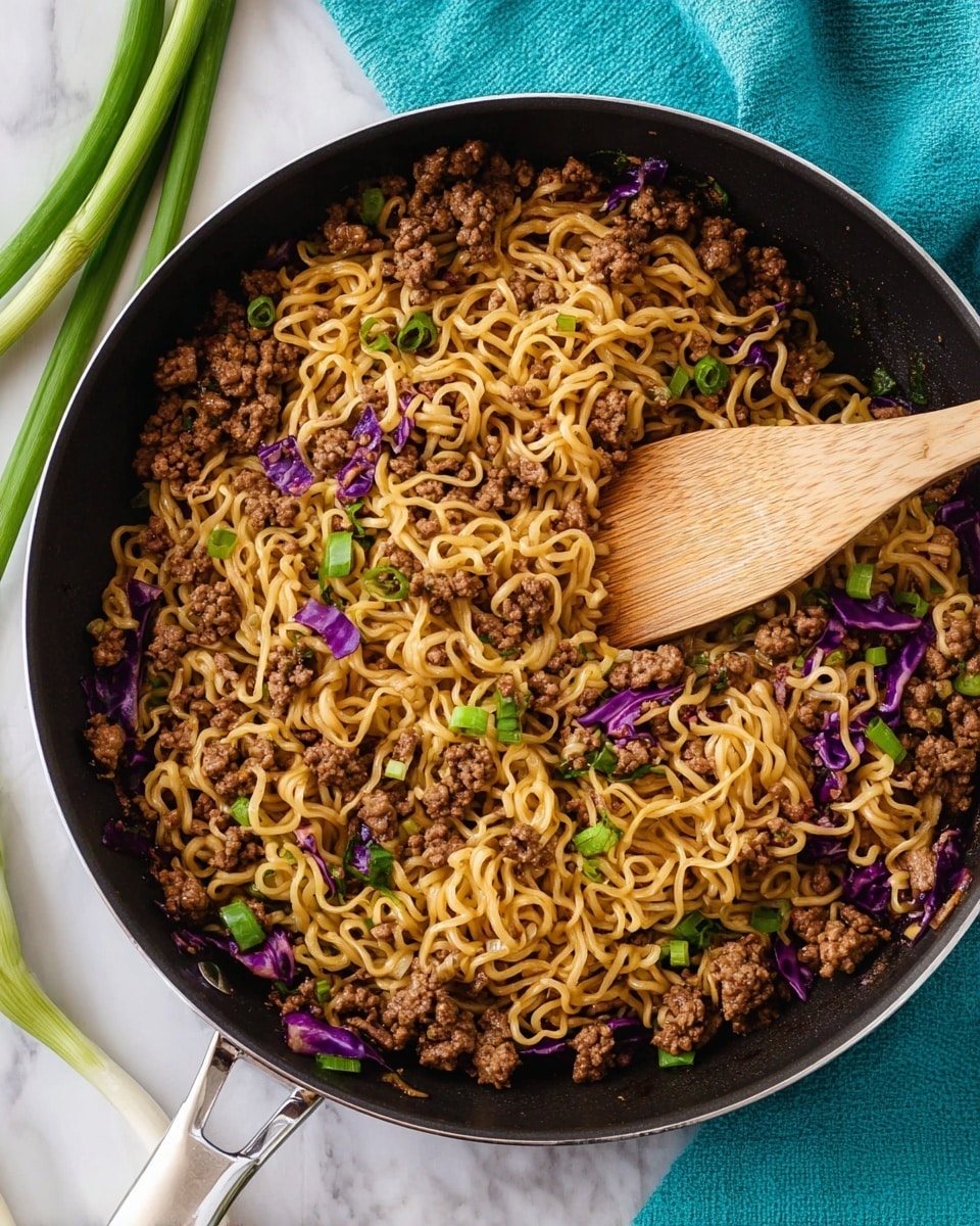The image shows a black skillet filled with a single layer of cooked yellow noodles mixed with browned ground meat, scattered pieces of purple cabbage, and bright green chopped scallions. A wooden spatula rests inside the skillet, partially covered with the noodle and meat mixture. The skillet is placed on a white marbled surface with a turquoise cloth napkin nearby, and some whole green scallions are visible on the left side. Photo taken with an iphone --ar 4:5 --v 7