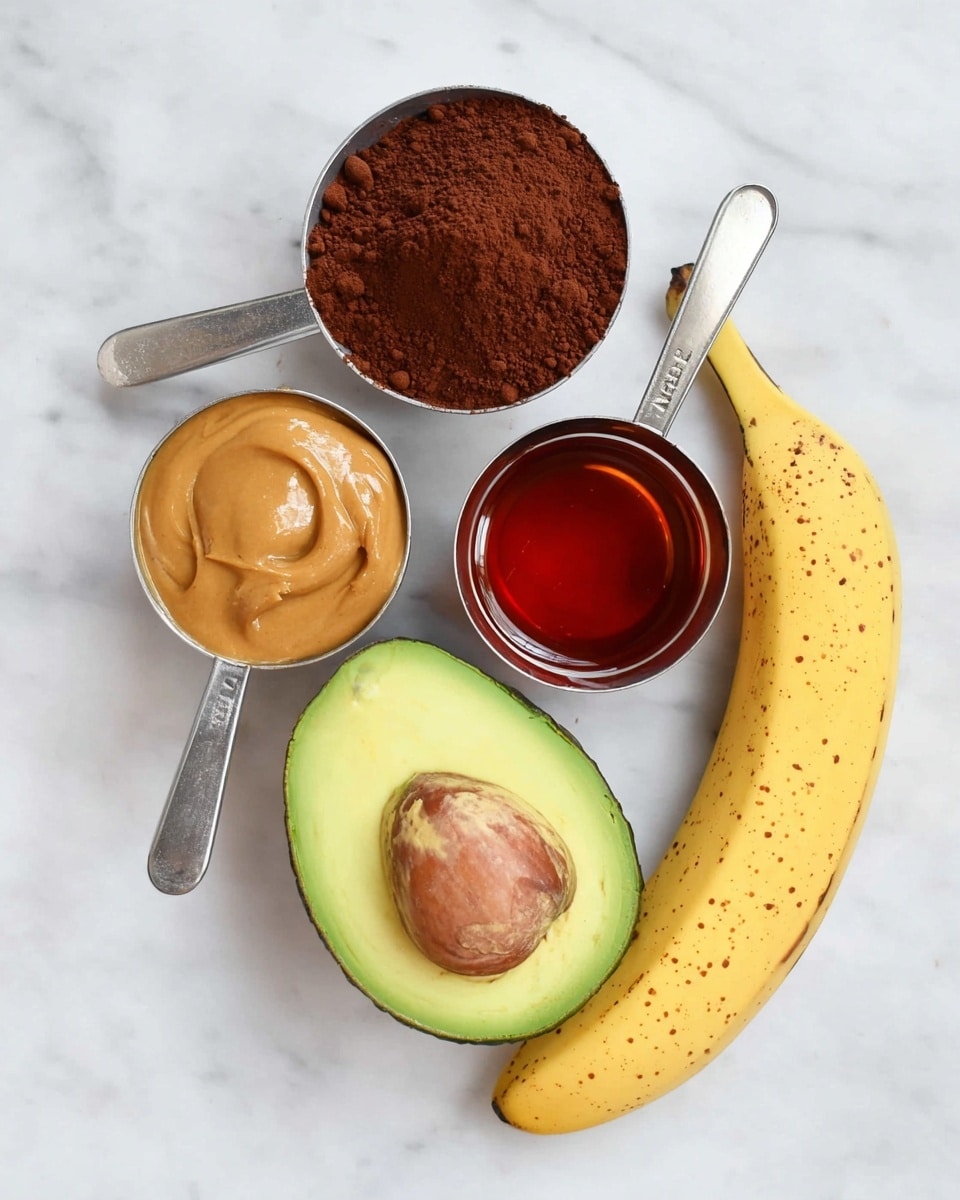 The image shows four measuring cups and two fruits on a white marbled surface. The top cup holds dark brown cocoa powder with a dry, crumbly texture. To the left below it, a cup contains smooth, light brown peanut butter. To the right of the cocoa powder, the third cup is filled with sticky, shiny reddish-brown liquid, possibly syrup. Near the cups, a halved avocado shows its bright green and yellow flesh with a large brown seed in the center, and a whole yellow banana with small brown spots is placed on the right side. The items are arranged in a flat lay style with good lighting. Photo taken with an iphone --ar 4:5 --v 7