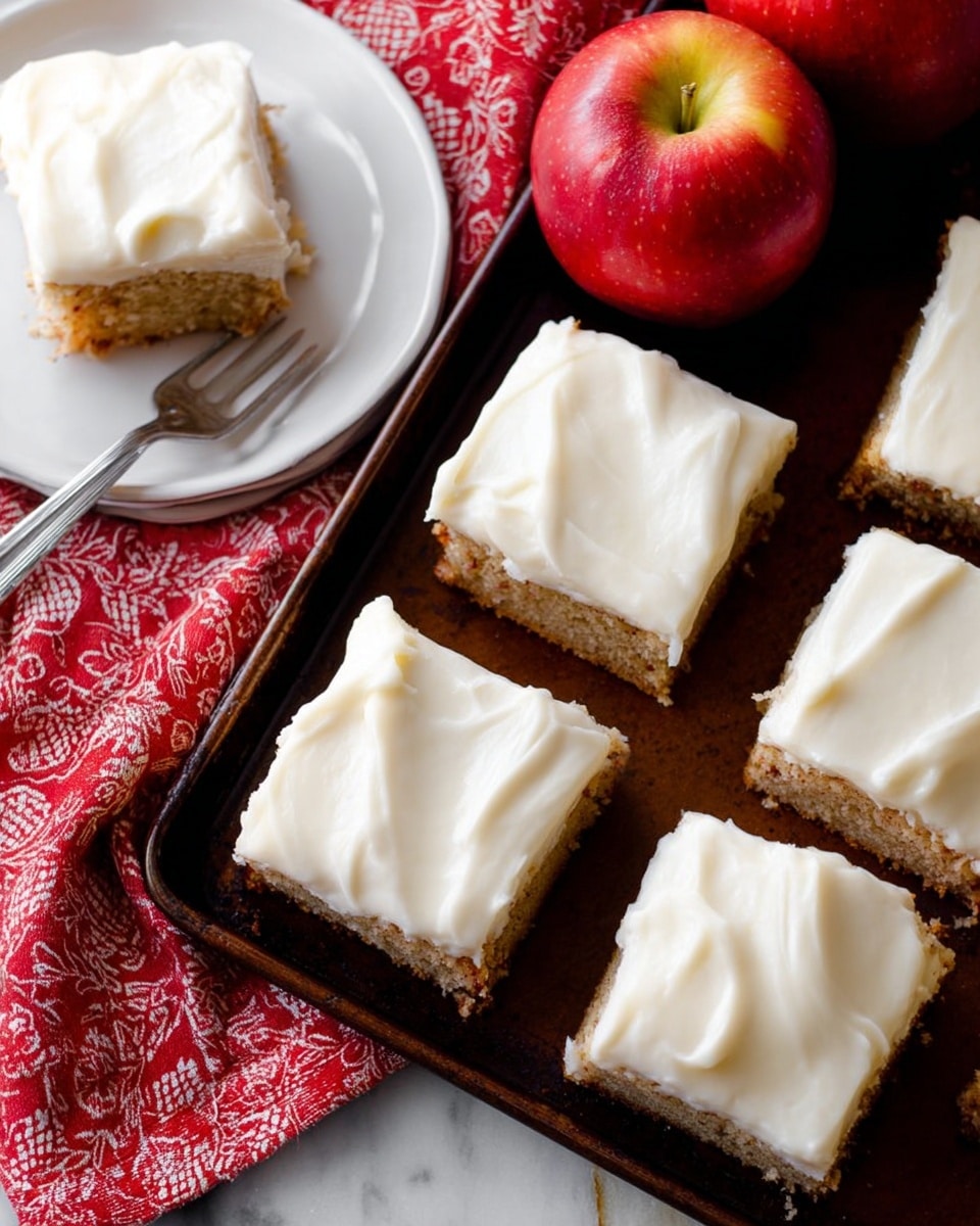 Six square pieces of cake topped with thick, creamy white frosting are arranged on a dark brown tray. The cake layers underneath look light brown and moist with a slightly rough texture. To the left side, there is a white plate on a red cloth with white patterns, holding one piece of cake with frosting and a silver fork resting on the plate. Two red apples with yellow streaks sit at the top of the tray. The whole scene is set on a white marbled textured surface. Photo taken with an iphone --ar 4:5 --v 7