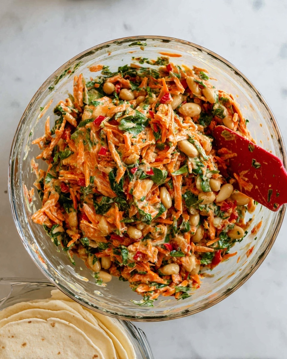 A clear glass bowl sits on a white marbled surface, filled with a colorful mixed salad. The salad has roughly three layers of ingredients blended together: bright orange shredded carrots, green chopped leafy vegetables, and light beige chunks that look like beans or nuts. There are also small pieces of red, possibly chopped tomatoes or peppers, mixed throughout. A red spatula is partly stuck into the mixture on the left side of the bowl. Below the bowl, partially visible, are white tortillas stacked in a second clear glass dish. The photo was taken with an iphone --ar 4:5 --v 7