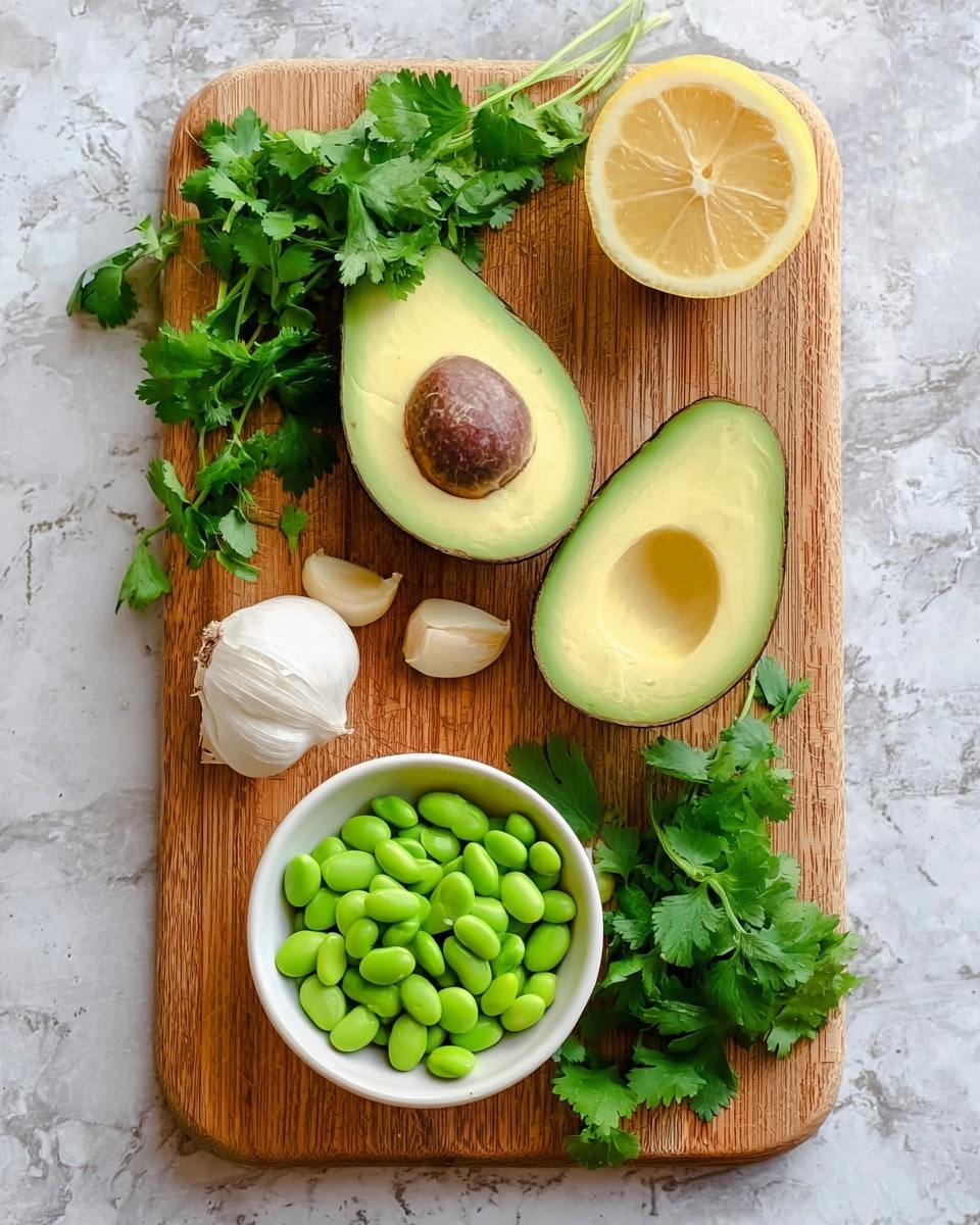 The image shows a wooden cutting board on a white marbled surface, with fresh green cilantro leaves spread across it. There are two halves of a ripe avocado placed near the center, one with the large brown seed and the other with the seed removed, revealing light green creamy flesh. A half lemon with a pale yellow inside is positioned near the top left, and a bulb of white garlic is at the bottom left. In the lower right part of the cutting board, a small white bowl is filled with bright green edamame beans. Photo taken with an iphone --ar 4:5 --v 7