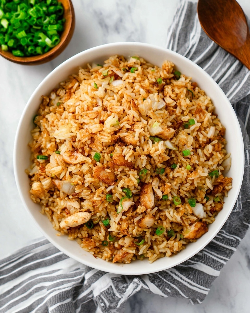 A white bowl filled with fried rice that has three main layers: the base layer is light brown rice mixed with small pieces of white chicken and lightly browned onion, the middle layer shows more grains of rice mixed with small bits of browned meat and onions, and the top layer is a heap of golden-brown fried rice pieces with chunks of white chicken and browned onions scattered throughout. The bowl rests on a white marbled surface next to a small wooden bowl filled with chopped green onions and a striped grey and white cloth napkin is nearby. Photo taken with an iphone --ar 4:5 --v 7