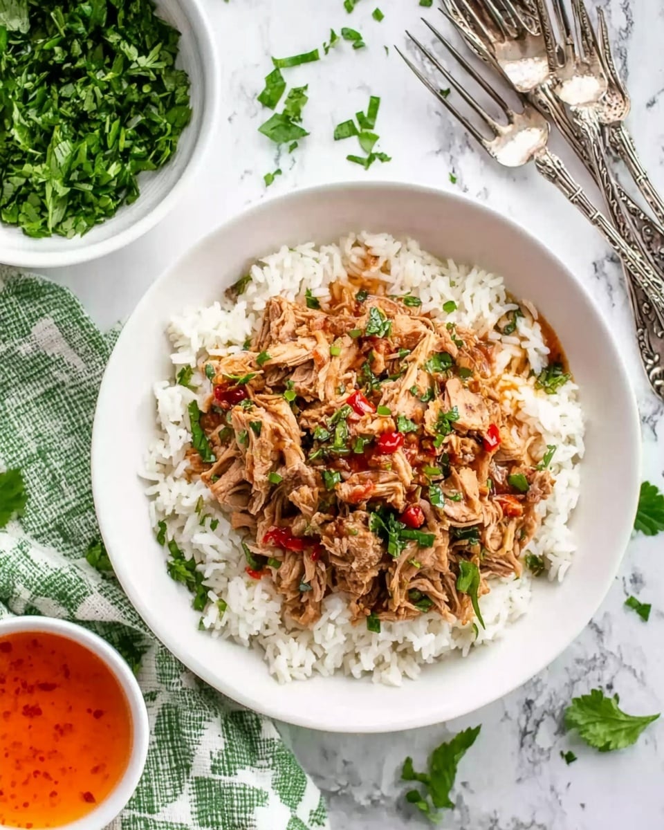 A white bowl filled with white rice at the bottom, topped with a layer of cooked shredded meat mixed with small green herbs and pieces of red chili. The bowl is placed on a white marbled surface with a few green herb leaves scattered around. To the left, there is a white bowl with fresh green chopped herbs and several silver forks with ornate handles resting on a green and white checkered cloth. In the bottom right, there is a small white bowl with bright orange sauce. The photo taken with an iphone --ar 4:5 --v 7