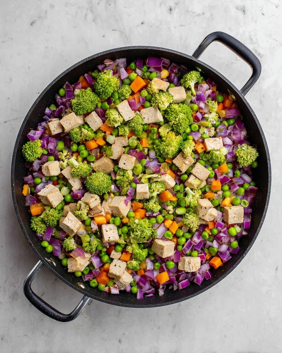 A black pan filled with a colorful mix of chopped vegetables and tofu pieces sits on a white marbled surface. The dish has a base layer of finely diced purple onions, bright green peas, and small orange carrot cubes evenly spread throughout. On top, there are many small, fresh broccoli florets in a vibrant green color scattered around. Adding more texture, there are medium-sized chunks of light brown tofu placed randomly over the vegetables. The pan has black handles and is viewed from above, showing a fresh, healthy mix of plant-based ingredients. photo taken with an iphone --ar 4:5 --v 7