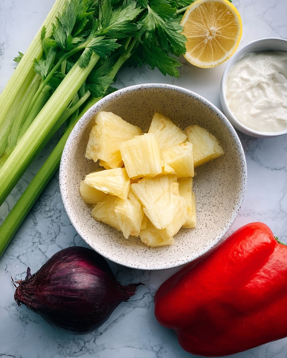 Yucca Salad (Cassava Salad) Recipe 4 A white speckled bowl filled with chunks of light yellow pineapple sits in the center on a white marbled surface. To the right of the bowl, a bright red bell pepper half rests, showing its smooth and shiny inner surface. Below the pepper, a dark purple onion with a rough texture lies close to three long, green celery stalks with fresh leafy tops extending towards the front of the image. Above the bowl, there is a half lemon showing its bright yellow, juicy interior, and a small round white bowl filled with creamy yogurt. photo taken with an iphone --ar 4:5 --v 7