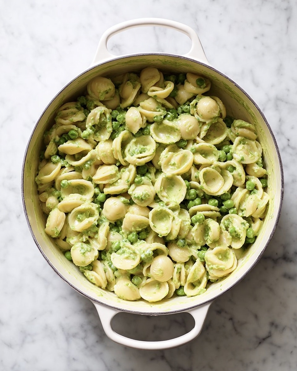 The image shows a white pot filled with orecchiette pasta mixed with green peas and a light green sauce. The pasta is round and slightly curved, filling the pot evenly. The peas add bright spots of green throughout the dish, and the sauce gives the pasta a smooth, slightly creamy texture. The pot is on a white marbled surface, and the scene is clear and bright. photo taken with an iphone --ar 4:5 --v 7