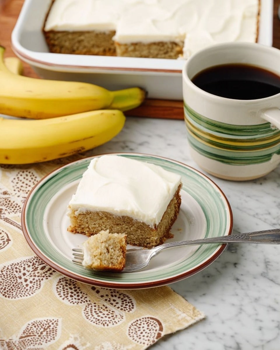 The image shows a square piece of banana cake with two layers: a light brown soft cake base and a thick, smooth white frosting layer on top, placed on a white plate with a green and brown rim. A small piece of the cake has been taken with a silver fork resting on the plate. In the background, there is a white rectangular baking pan with more banana cake which also has the white frosting layer. To the left of the plate, two bananas sit on a beige napkin with brown circular patterns, all on a white marbled surface. To the right, there is a white ceramic mug with green and brown horizontal stripes filled with black coffee. photo taken with an iphone --ar 4:5 --v 7