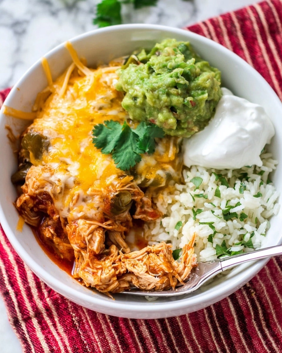 A white bowl holds a layered dish with shredded cooked chicken covered in melted yellow cheese and a reddish sauce on the left side. Above it, there is a scoop of bright green guacamole topped with a fresh cilantro leaf. To the right of the guacamole, there is a dollop of white sour cream also garnished with a cilantro leaf. On the far right, there is a pile of white rice mixed with small green herbs next to a small portion of shredded white and yellow cheese. A silver fork rests on the bottom right edge of the bowl with a small piece of the chicken mixture on its prongs. The bowl sits on a red and beige striped cloth on a white marbled surface. Photo taken with an iphone --ar 4:5 --v 7