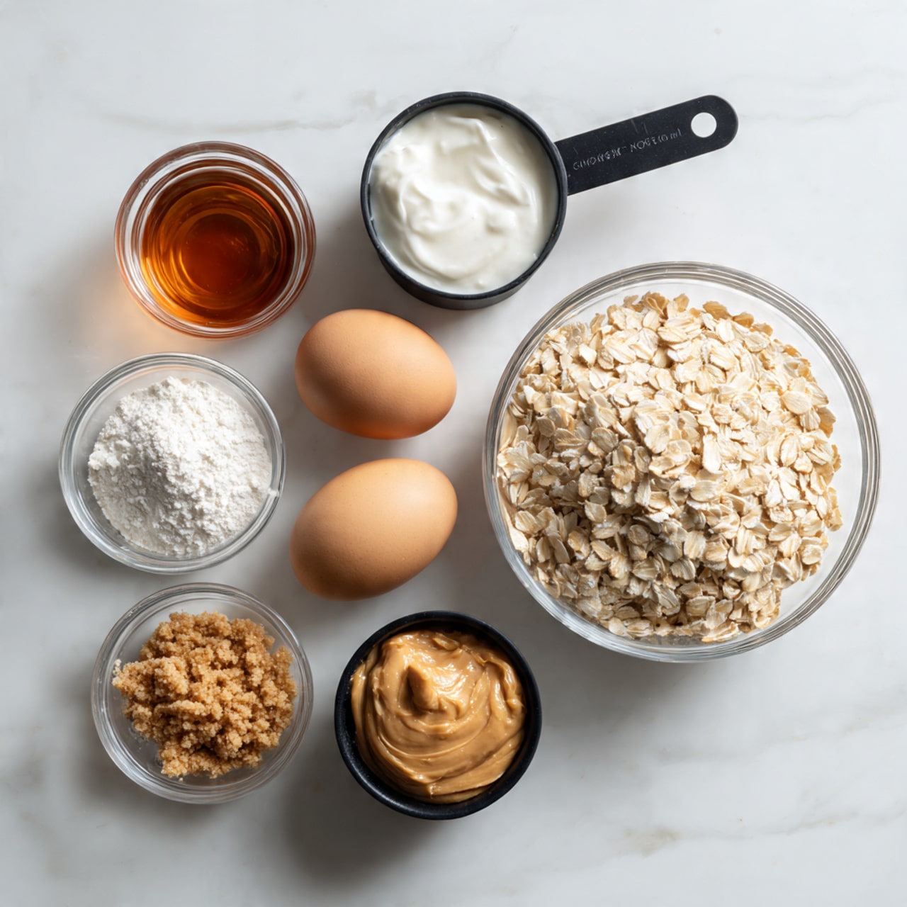 The image shows seven separate small containers of ingredients arranged on a white marbled surface. There is a clear glass bowl full of light tan rolled oats placed on the right side. Next to it, a black measuring cup holds a thick white creamy substance. Two light brown eggs lie together below the bowl of oats. A small glass jar of dark amber liquid is positioned near the top left. Below the eggs, a small clear glass bowl contains white powder. Another small clear glass bowl holds a coarse brown ground substance placed to the bottom left. Lastly, a black measuring cup filled with light brown peanut butter is placed near the bottom right. All the containers and ingredients are neatly spaced out. Photo taken with an iphone --ar 4:5 --v 7