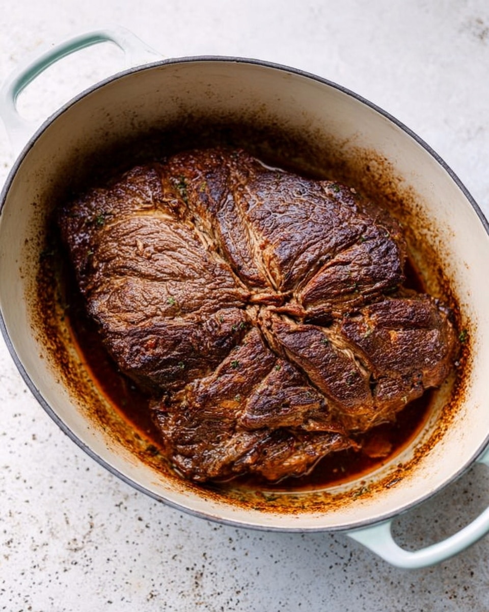 The image shows a large piece of cooked meat with a dark brown crust, sitting in a white oval pot with two handles on a white marbled surface. The meat has a textured surface with some visible lines and cracks, and it fills most of the pot, which has browned juices around the edges. The pot is placed on a light speckled background, contrasting with the rich, browned color of the meat. Photo taken with an iphone --ar 4:5 --v 7