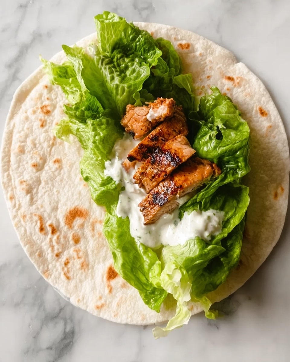 The image shows one flat white tortilla on a white marbled surface, topped with layers of green lettuce leaves that are fresh and soft. On top of the lettuce, there is a piece of grilled meat with a golden-brown texture and some char marks. There is also a dollop of white sauce spread on the meat, adding a creamy texture. The dish looks fresh and ready to be wrapped or eaten as is. photo taken with an iphone --ar 4:5 --v 7
