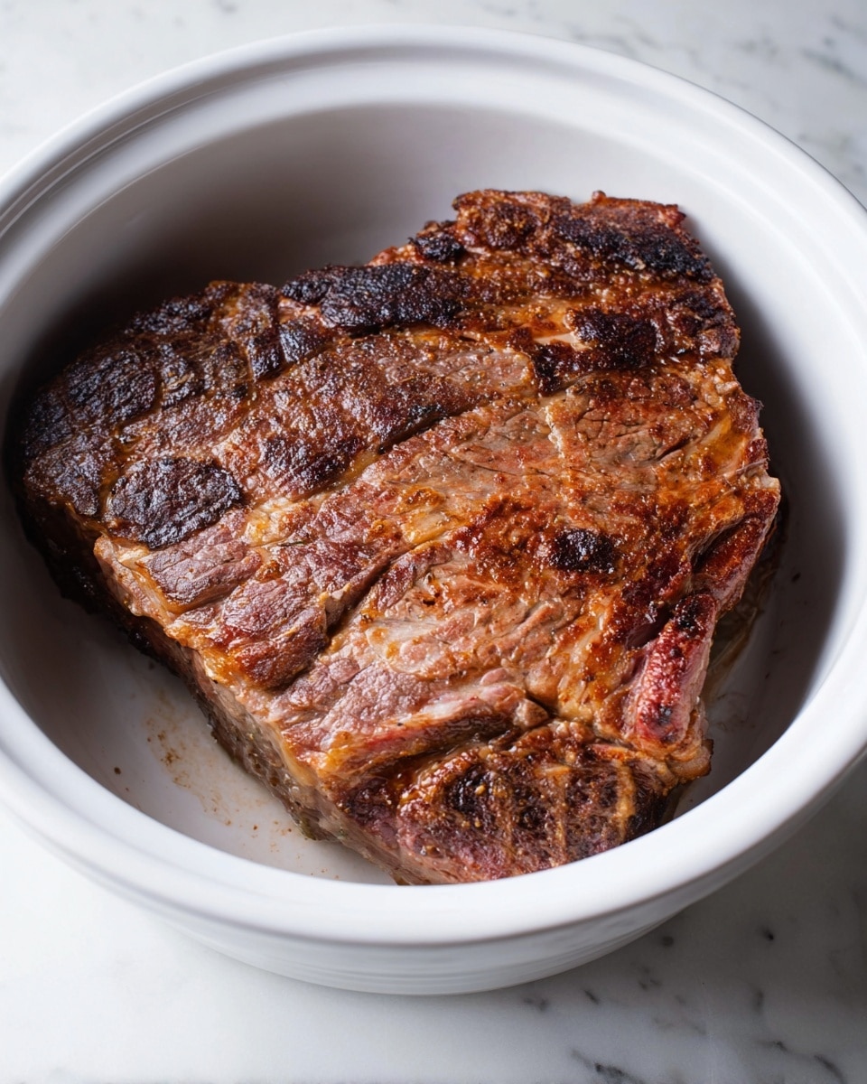 A single thick piece of cooked meat sits in a large white bowl, showing a browned and slightly crispy surface with a mix of dark and light brown shades. The meat has a textured look, with visible grill marks and some charred edges. The inside has slightly pink areas, giving it a tender touch. The bowl is placed on a surface with white marbled texture. photo taken with an iphone --ar 4:5 --v 7