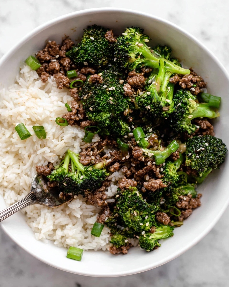 A white bowl contains two main layers: on the left side, a bed of white steamed rice topped with small green onion slices and sesame seeds; on the right side, a mix of cooked ground beef and bright green broccoli florets, both with a slightly shiny texture from sauce, scattered with sesame seeds and small chopped onions. A silver fork is lifting a bite with broccoli and rice from the bowl. The bowl rests on a white marbled surface. photo taken with an iphone --ar 4:5 --v 7