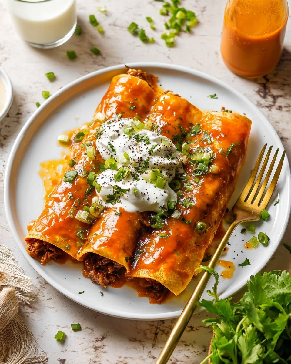 Three rolled orange tortillas filled with dark meat and placed side by side on a white plate, each covered in a thick, shiny orange sauce. On top of the middle two tortillas, there are two white dollops of sour cream sprinkled with black pepper and green herbs. Green chopped herbs and scallions are scattered on and around the tortillas. A small bunch of fresh leafy green herbs sits to the right side of the plate next to a golden fork. The plate is set on a white marbled surface with a glass of a white creamy drink and a small glass bottle of orange sauce blurred in the background. photo taken with an iphone --ar 4:5 --v 7