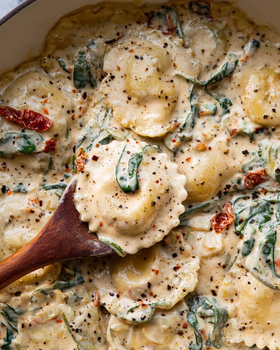 The image shows round ravioli pasta pieces with a doubled-edge design, covered in a thick, creamy white sauce speckled with black pepper and herbs. Mixed in the sauce are dark green leafy bits, likely spinach, and small red pieces, possibly sun-dried tomatoes, adding spots of color. The sauce has a smooth and slightly chunky texture with visible flecks of seasoning throughout. A wooden spoon is partly submerged in the creamy mixture, holding one piece of ravioli. The background is a close-up of the dish with a white marbled surface barely visible around the edges. Photo taken with an iphone --ar 4:5 --v 7