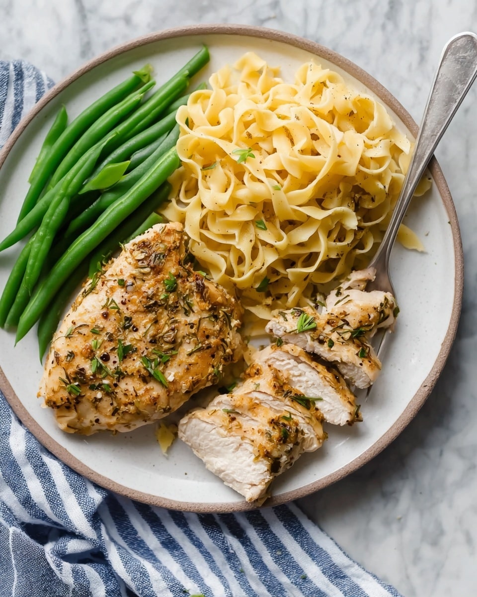 A round white plate is placed on a white marbled surface with a blue and white striped cloth beside it. The plate holds three main layers: on the left side, there are bright green whole green beans arranged in a small bunch; next to them, in the upper middle part of the plate, is a generous pile of lightly yellow cooked egg noodles with a smooth and soft texture, loosely stacked; on the right side, two pieces of baked chicken with a golden brown color, seasoned with herbs and small bits of garlic, lie flat with one piece slightly sliced to reveal the plain white inside. A silver fork with some noodles wrapped on its tines rests near the top right edge of the plate. Photo taken with an iphone --ar 4:5 --v 7