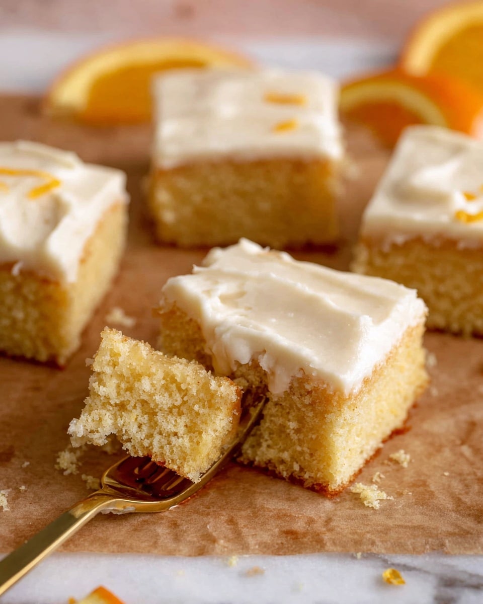 Several square pieces of light golden cake with a soft, porous texture are shown on brown parchment paper over a white marbled surface. Each square has one thick layer of smooth, creamy white frosting on top. A gold fork with a piece of cake and frosting is placed in the front left, showing a close-up of the cake's crumbly texture. Part of an orange slice is visible on the right side. The background is softly blurred, focusing on the cake pieces and the fork. Photo taken with an iphone --ar 4:5 --v 7