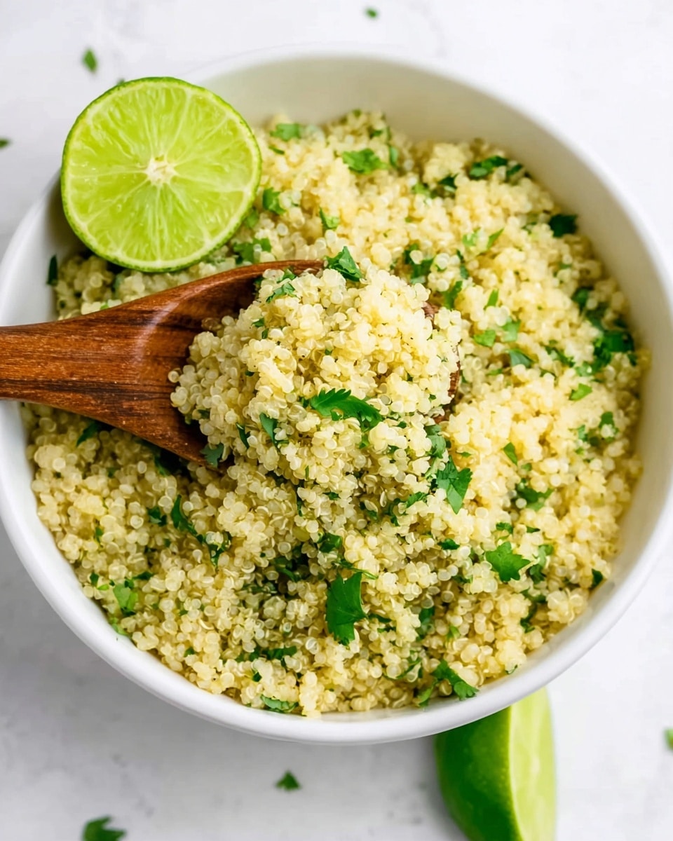 A bowl filled with a fluffy light yellow quinoa mix with small green cilantro leaves scattered throughout. A wooden spoon rests inside the bowl on the left side, partially lifting some quinoa. Around the bowl sit two lime halves with a vibrant green color. The bowl is white, placed on a white marbled surface, adding a clean and fresh feel to the image. Photo taken with an iphone --ar 4:5 --v 7