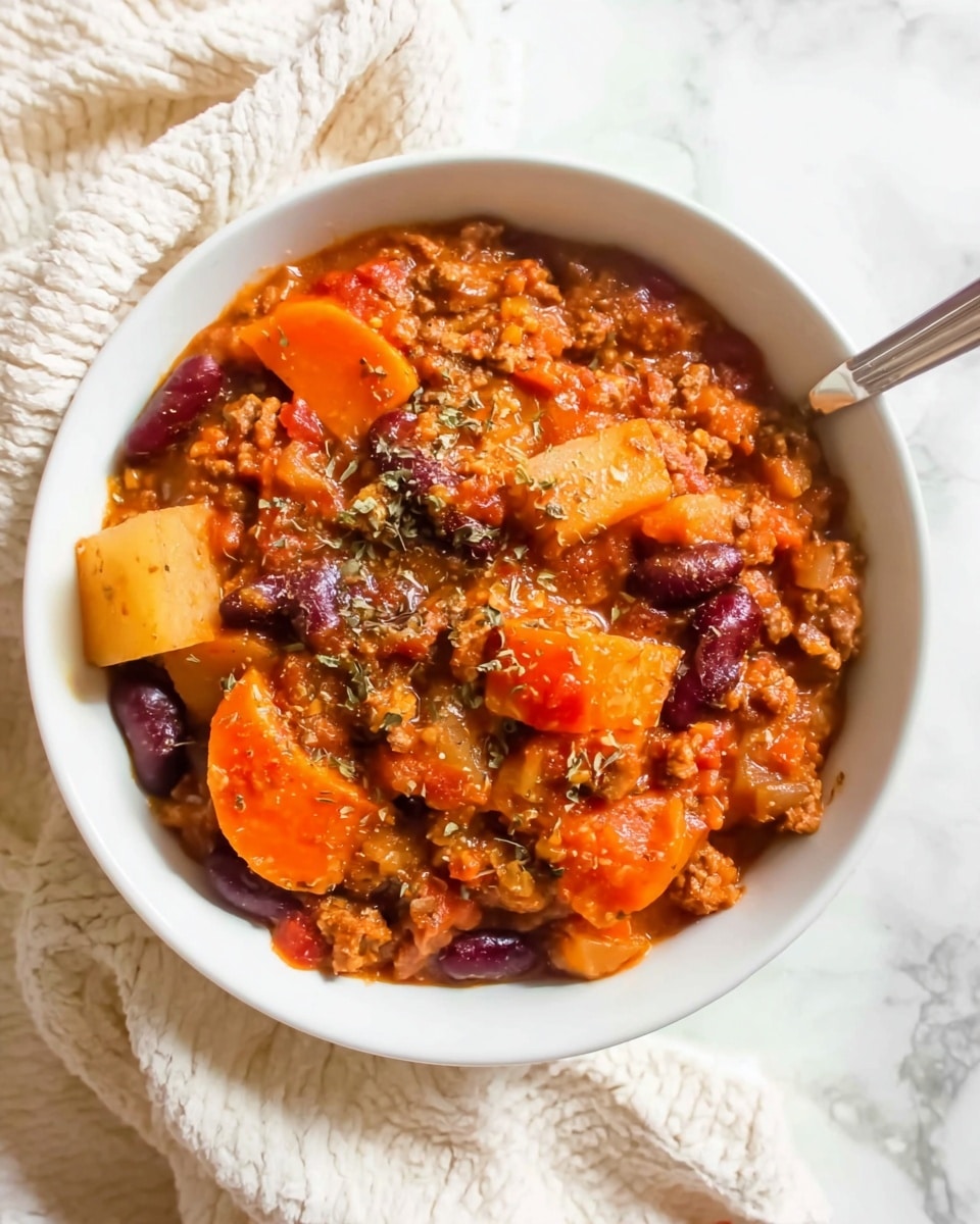 A white bowl filled with a thick mix of hearty stew showing a few layers of chunky orange carrot slices, yellow potato cubes, dark red kidney beans, and small pieces of ground meat, all cooked in a rich orange-red sauce with bits of herbs sprinkled on top. The textures vary from smooth sauce to soft vegetable chunks, and the bowl is set on a white marbled surface with a cream-colored textured cloth nearby, with a spoon partly visible inside the bowl. Photo taken with an iphone --ar 4:5 --v 7