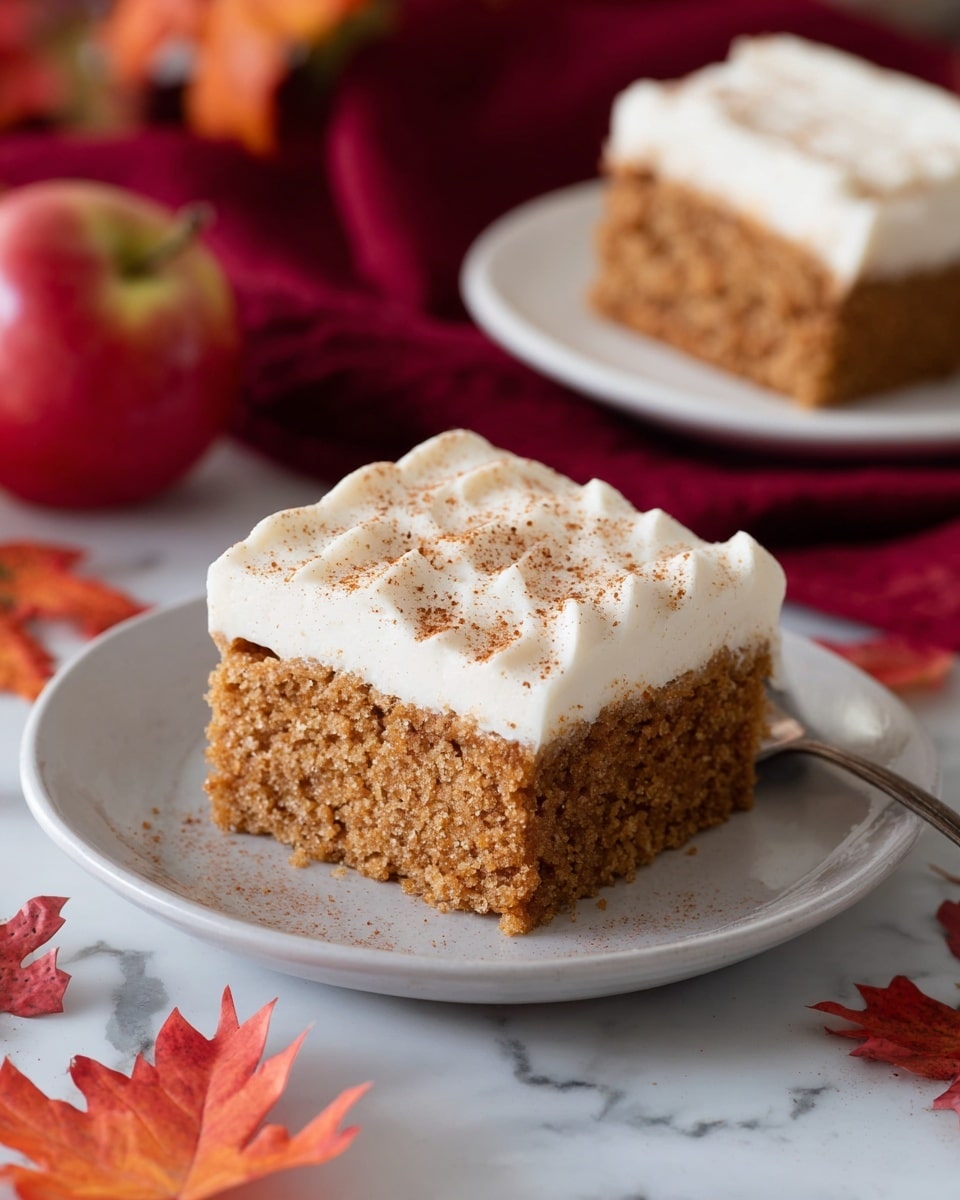 A square piece of two-layer cake is shown on a white plate, sitting on a white marbled surface. The bottom layer is a thick, soft-looking, light brown cake with a crumbly texture. On top is a thick, smooth white frosting layer with gentle, wavy grooves and a light sprinkle of cinnamon or similar spice on the surface. In the background, there is another piece of the same cake on a white plate, a red apple, and some red and orange autumn leaves scattered around, with a red cloth nearby. Photo taken with an iphone --ar 4:5 --v 7