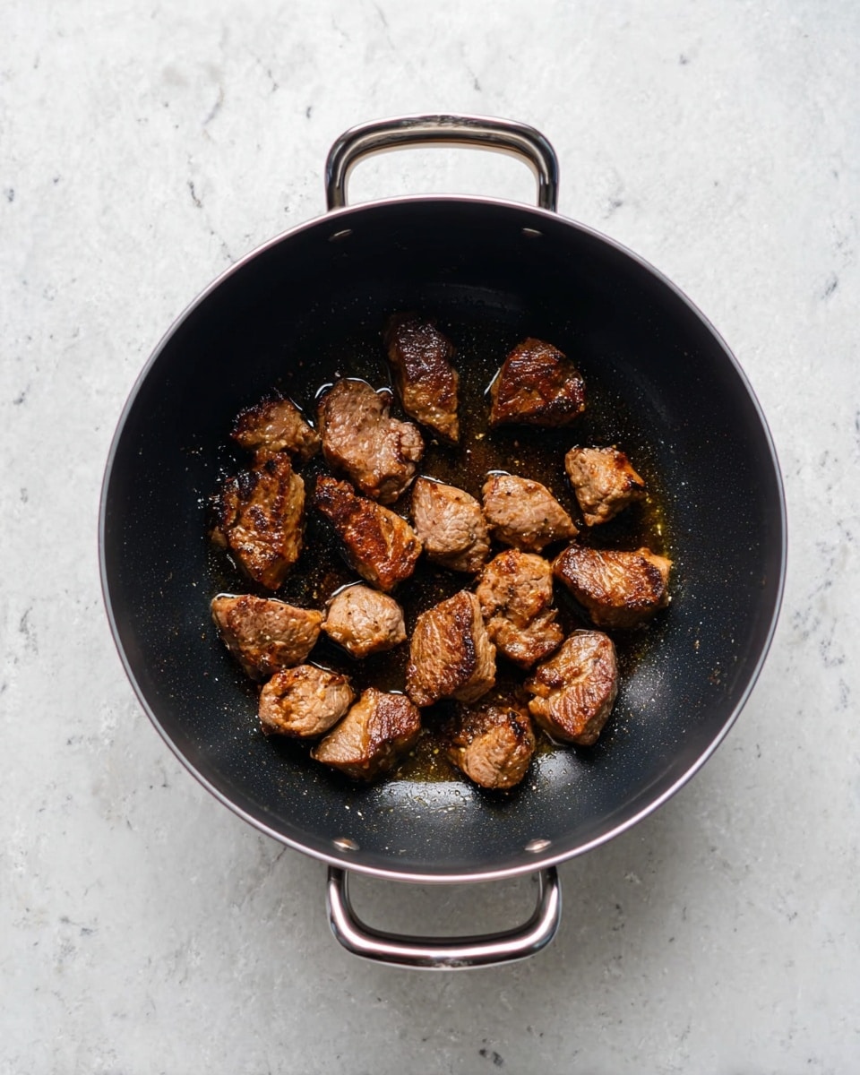 A black pot filled with ten small, browned pieces of cooked meat spread evenly inside, showing a lightly crisp texture with some oil shine on the bottom. The pot has two handles and sits on a white marbled surface, providing a clean and simple background that highlights the dark pot and meat pieces. The meat pieces have a mix of golden-brown and darker seared parts, arranged loosely without overlapping, emphasizing their individual shapes and textures. Photo taken with an iphone --ar 4:5 --v 7
