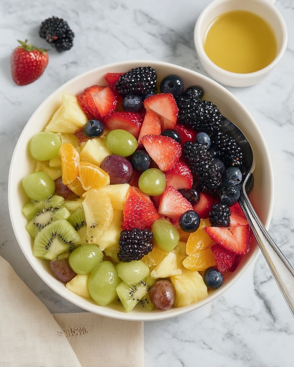 A white bowl filled with a vibrant fruit salad featuring several layers of colorful fruit pieces. The base layer includes green grapes and red grapes cut in halves, along with chunks of pale yellow pineapple. On top of this, there is a mix of sliced green kiwi and orange mandarin segments scattered evenly. The upper layer has fresh strawberry slices with bright red color, plump blackberries with deep black-purple skin, and scattered dark blue blueberries, creating a rich contrast of colors and textures. A silver spoon rests inside the bowl on the right side, with the bowl placed on a white marbled surface next to a white small bowl holding light yellow honey. Photo taken with an iphone --ar 4:5 --v 7