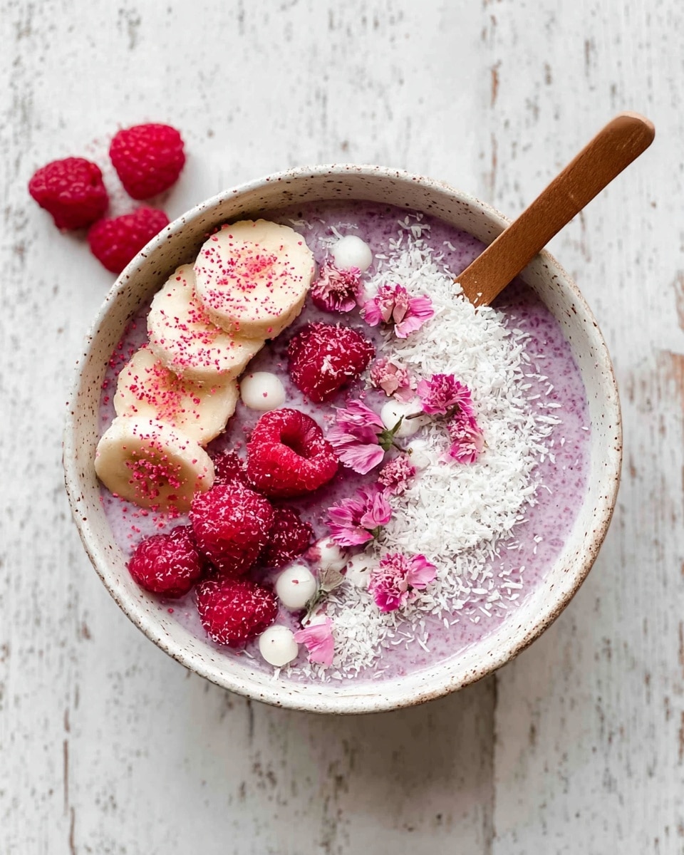 A white speckled bowl filled with a light purple chia pudding base that covers the entire inside. On top, to the left, there are three banana slices sprinkled with pink powder and small white crunchy balls scattered around. The banana slices are partially covered with shredded white coconut flakes that continue around the edge of the bowl. To the right center, there is a cluster of bright red raspberries, some whole and some showing their hollow insides. Small delicate pink flower petals are placed near the raspberries, adding a soft touch. A wooden spoon is resting inside the bowl, angled towards the top left. The bowl is set on a white marbled textured surface with a few raspberries nearby. photo taken with an iphone --ar 4:5 --v 7