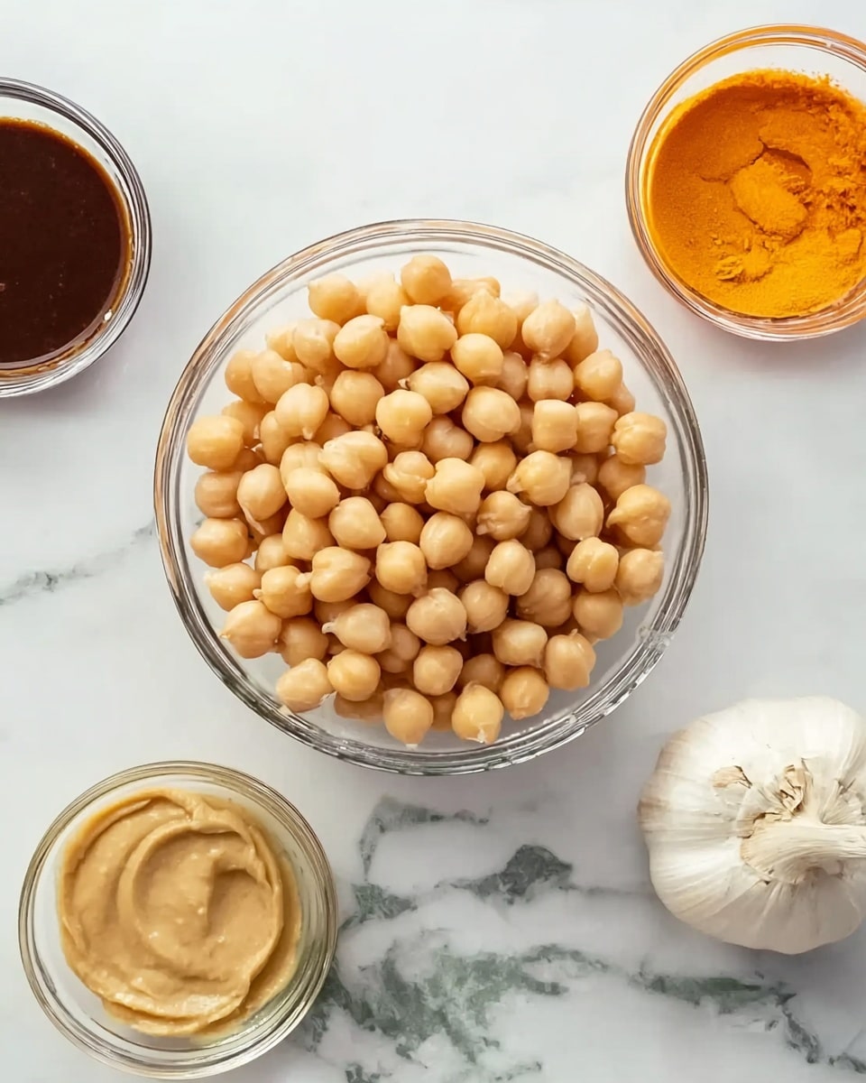 The image shows a clear glass bowl filled with light beige chickpeas that look smooth and round, placed on a white marbled surface. Around the bowl, there are four smaller clear glass bowls with different sauces and spices: one contains a thick dark brown sauce, another holds a light tan creamy sauce, a third has a bright orange sauce with a slightly shiny texture, and the last one shows part of a whole garlic bulb with white papery skin and a bit of its root visible. All items are spaced evenly on the white marbled surface. Photo taken with an iphone --ar 4:5 --v 7