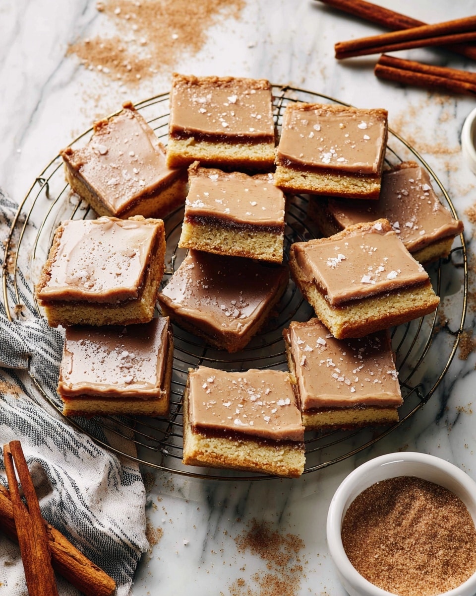 The image shows a batch of square cinnamon bars arranged on a round wire rack. Each bar has two visible layers: a thick, light golden cookie base with a middle dark brown cinnamon filling, topped with a smooth, light brown cinnamon glaze sprinkled with coarse salt flakes. Some bars are whole, and a few are stacked or showing their side layers. The wire rack rests on a white marbled surface with scattered brown sugar, cinnamon sticks, and a white bowl filled with brown sugar and cinnamon sticks visible in the corner. A piece of striped cloth is partly visible underneath the setup. Photo taken with an iphone --ar 4:5 --v 7