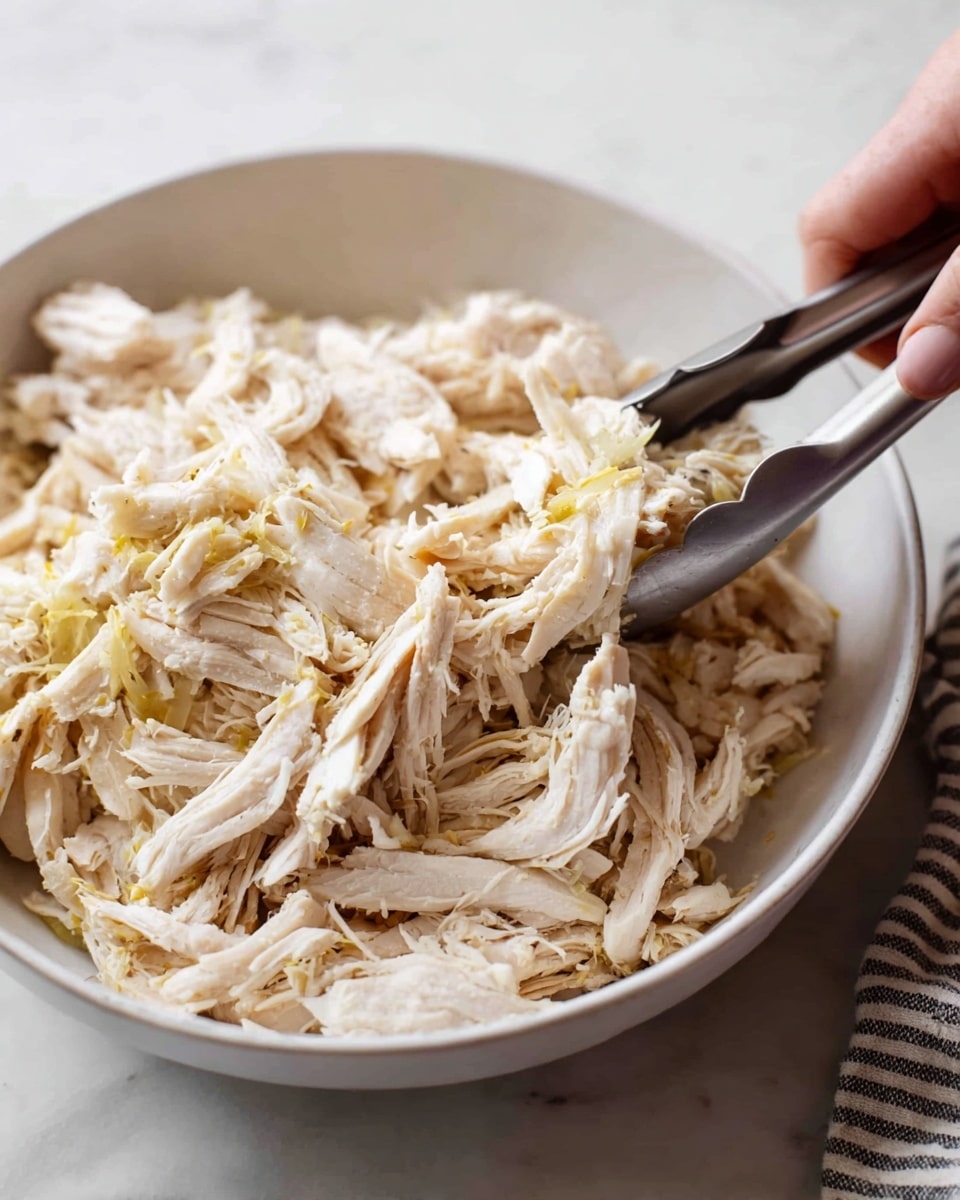 The image shows a close-up top view of an instant pot filled with shredded pale yellowish-white cooked chicken mixed with some light green pieces of cooked peppers or similar vegetables. The mixture rests inside the shiny metal inner pot, which is placed in a black outer casing. The background is a white marbled surface. photo taken with an iphone --ar 4:5 --v 7