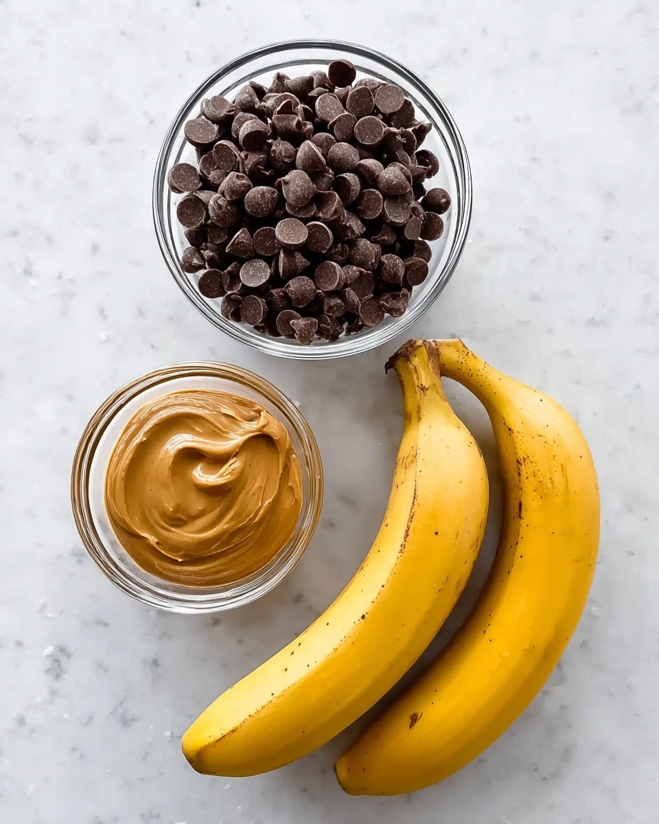 The image shows three main items placed on a white marbled surface: a clear glass bowl filled with dark brown chocolate chips in the top center, a smaller clear glass bowl containing smooth light brown peanut butter in the lower left, and two ripe yellow bananas with a few brown spots positioned in the lower right, slightly angled towards the bowls. photo taken with an iphone --ar 4:5 --v 7