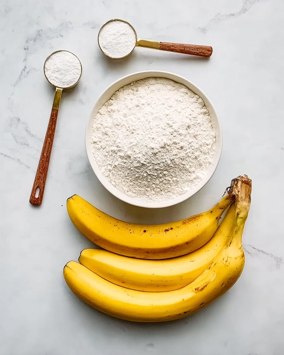 The image shows a white bowl filled with white flour in the center on a white marbled surface. Below the bowl, there are three ripe yellow bananas with a few brown spots arranged side by side. Above the bowl, there are two measuring spoons with wooden handles, one larger and one smaller, with white powder or sugar inside. The scene is simple and bright with natural lighting. Photo taken with an iphone --ar 4:5 --v 7
