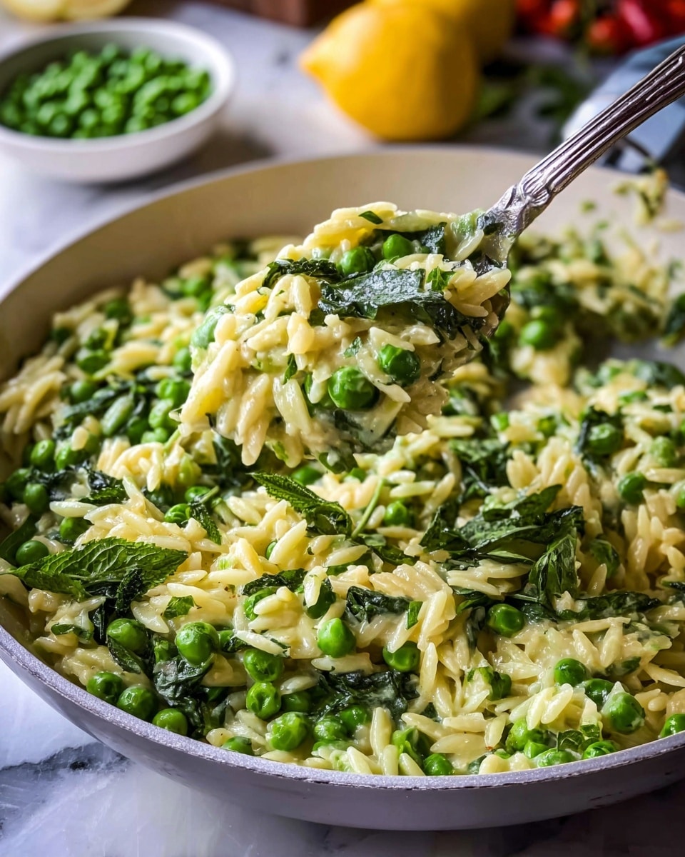 The dish shows a creamy orzo pasta mixed with bright green peas and fresh leafy herbs, likely spinach and mint, all cooked together in a white skillet. The orzo grains are soft with a pale yellow creamy coating, spread evenly with the peas scattered throughout and the green leaves lying on top and mixed inside. A silver spoon is lifting a portion, showing the texture and combination of rice-like pasta, peas, and herbs. The scene is set on a white marbled surface with fresh green peas in a small white bowl and yellow vegetables blurred in the background. photo taken with an iphone --ar 4:5 --v 7