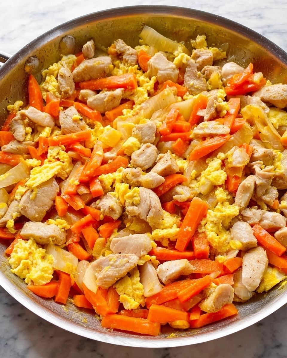 A close-up image showing a round silver pan with cooked pieces of chicken, bright orange carrot chunks, and soft scrambled eggs mixed together. The chicken pieces are light beige with a slightly textured surface, scattered evenly throughout the pan. The carrots are cut into small thick sticks, their vibrant orange color standing out among the pale chicken and yellow eggs, which have a soft, fluffy texture with some small curds. The pan rests on a white marbled surface, and the lighting highlights the freshness and warmth of the cooked ingredients. photo taken with an iphone --ar 4:5 --v 7