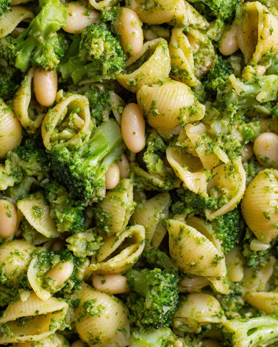 The dish shows small shell-shaped pasta mixed with small broccoli florets and white beans, all covered in a green sauce that looks like pesto. The pasta is a light yellow color, the broccoli is bright green, and the beans are pale cream. The textures vary, with the pasta looking soft, the broccoli slightly crisp, and the beans smooth. Everything is evenly mixed, creating a close-up view of the ingredients blending together, with no visible plate or bowl edges and a tight focus on the food. Photo taken with an iphone --ar 4:5 --v 7