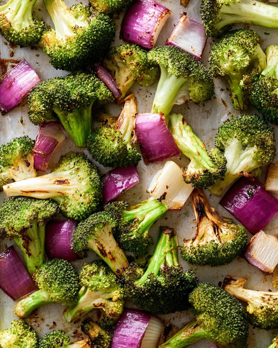 The image shows a close-up of roasted broccoli and red onion pieces scattered on a baking tray. The broccoli florets are bright green with some parts slightly charred, showing a textured surface with small buds on top and thick light green stems. The red onion pieces are cut into large chunks with a purple outer skin and white inner layers, some edges slightly browned from roasting. The background is a white marbled texture seen around the edges of the tray, adding contrast to the vibrant green and purple colors of the vegetables. photo taken with an iphone --ar 4:5 --v 7